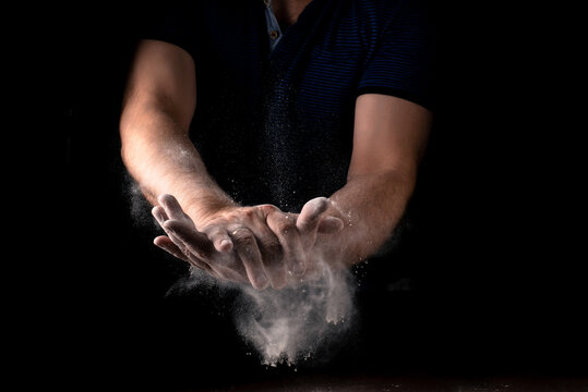 A cloud of flour scatters from male hands on a black background. Cooking concept. © Konstiantyn Zapylaie