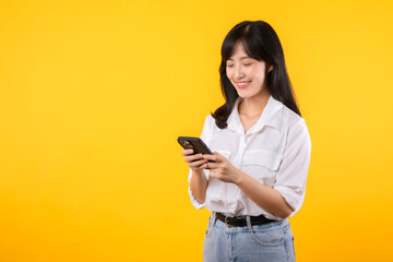 Portrait beautiful young asian woman happy smile wearing white shirt and denim plants using smartphone isolated on yellow studio background. reading news from smartphone concept.