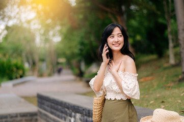 Portrait of asian young woman traveler with weaving hat, basket, mobile phone and camera on green public park background. Journey trip lifestyle, world travel explorer or Asia summer tourism concept.