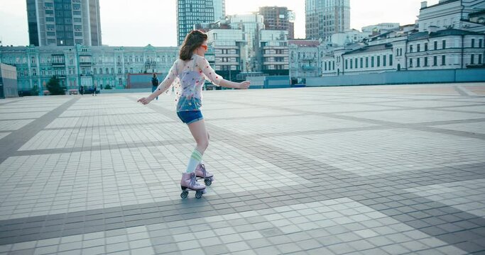 Young fit woman on roller skates riding outdoors on urban street. Smiling girl with rollerblading on sunny day