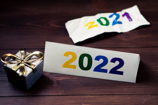 2022 numbers and crumpled 2021 of the outgoing year and new year gift on wooden background.
