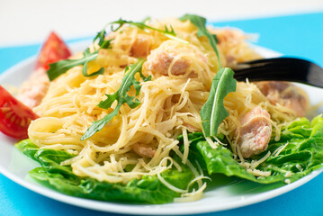 Spaghetti with salmon, cheese on a lettuce salad sprinkled with arugula and cherry tomatoes close-up.