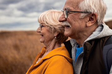 Active senior couple with backpacks hiking together in nature on autumn day..