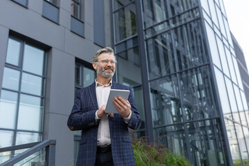 Successful gray-haired businessman smiling and happy, man using tablet computer, senior boss...