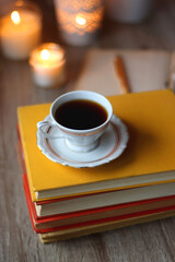 Cup of tea or coffee, plate of cookies, books, e-reader, pencil and lit candles on the table. Selective focus.