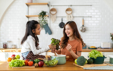 Portrait of enjoy happy love asian family mother and little asian girl daughter child having fun help cooking food healthy eat together with fresh vegetable salad and ingredient in kitchen