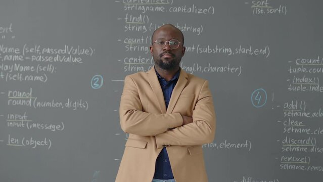 Medium portrait of male African American teacher coming to blackboard posing for camera in programming classroom at daytime