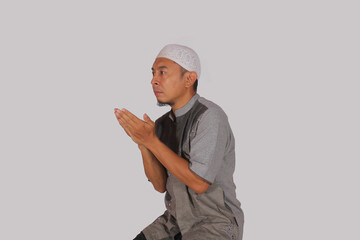 an Asian man in Muslim clothes is raising his hand with a certain symbol with a smile expression,asking for prayer
