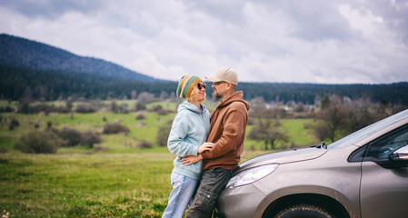 Romantic happy middle age couple hugging standing next to cars during auto travel in mountains