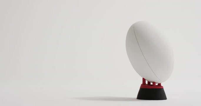 White rugby ball on kicking tee on white background with copy space, slow motion