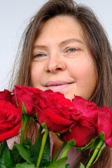 Fototapeta premium happy romantic mature woman with long hair holding bouquet of red roses in her hands, looking thoughtfully, concept skin care, age-related changes, procedures, care products, cosmetics