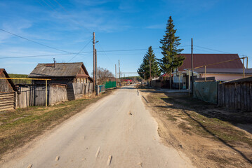 Fototapeta na wymiar dirt road in the village on the background of houses and pines