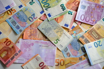 Obraz premium closeup paper 5,100, 50 euro banknotes of european union against background of scattered paper banknotes on table, concept of payments, savings, banking, save up for vacation, cash out currency