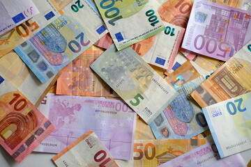 closeup paper 5,100, 50 euro banknotes of european union against background of scattered paper banknotes on table, concept of payments, savings, banking, save up for vacation, cash out currency