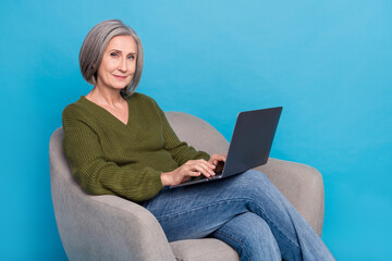 Naklejka premium Photo of good mood cheerful person wear knit pullover sitting in armchair with laptop write letter isolated on blue color background
