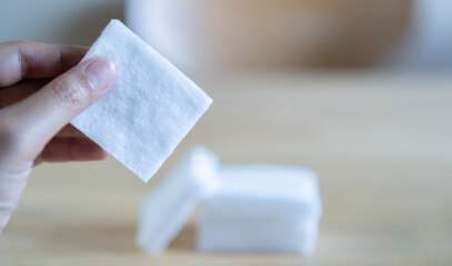 Cropped image of woman hand holding a cotton pad with blurred image of cottons stack on wooden table background. © Kunlathida