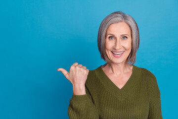 Photo of attractive pensioner lady direct finger empty space shopping offer wear khaki pullover isolated blue color background
