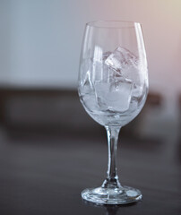 Ice cubes in an empty glass wine on a wooden bar counter, soft light background