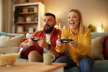Couple sitting on couch with joysticks and playing video game in living room