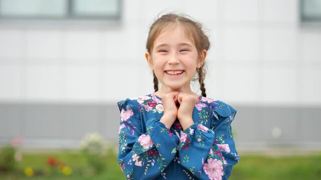 Junior school girl in flowery dress smiling on modern school background. Long haired girl with braids enjoying summer vacation at school camp