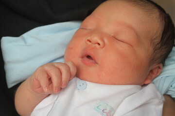 Portrait of a newborn boy who sleeps sweetly and smiles in he sleep in red clothes at a photo shoot of newborns

