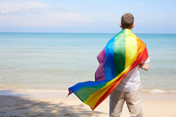 back young man looking to the sea and holding a rainbow flag(LGBT) on a tropical beach
