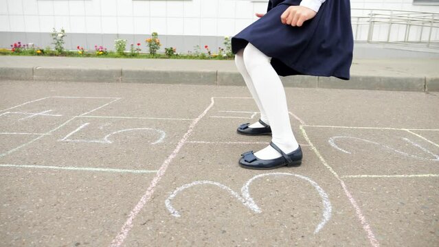 Junior school girl playing hopscotch in empty schoolyard. Student girl in uniform enjoys playing and jumping alone at school, close-up