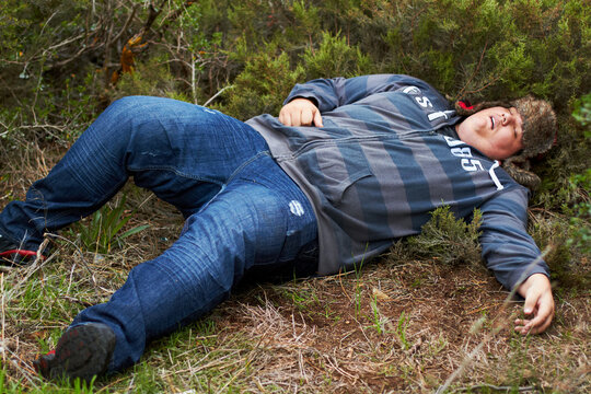 Drunk, sleeping and hangover with a plus size man lying outdoor on the grass or ground after a party. Festival, alcohol and tired with a young male person asleep on a field or lawn in the morning