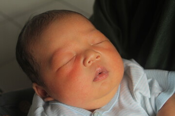 Portrait of a newborn boy who sleeps sweetly and smiles in he sleep in red clothes at a photo shoot of newborns
