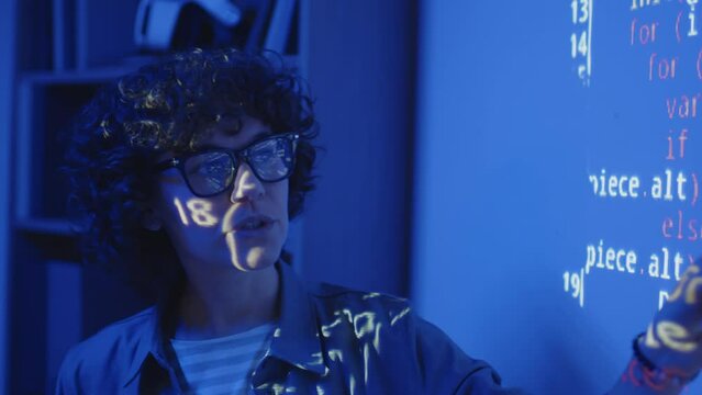 Close up of female Caucasian teacher standing in front of screen projection explaining code in dark classroom with blue light