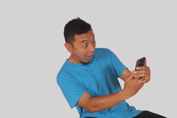 Asian mature man standing with surprised and serious expression while holding mobile phone
