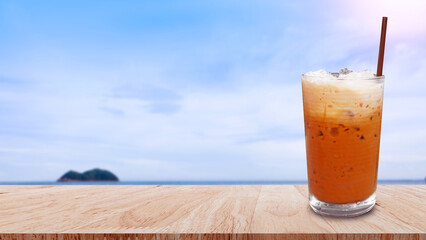 Iced thai milk tea in glass, Milk ice tea, Cheddar is a traditional Thai drink on wooden table with beach landscape nature background, Summer drinks with iced
