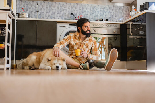 man with amputated leg prosthesis, at home with his dog, sitting in the kitchen while holding a cup of hot drink