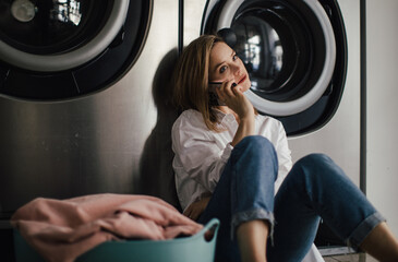 Fototapeta na wymiar Young woman calling, waiting in a laundry room.