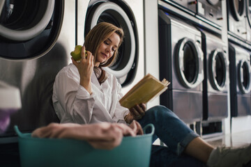 Young woman reading a book, waiting in a laundry room.