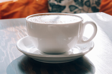 Cup of coffee on the wooden table in the cafe. Hard shadows, sunlight.