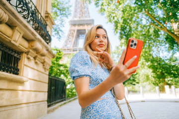 Young attractive woman making selfie photo using mobile phone near Eiffel Tower in Paris France, Woman tourist travelling on Europe  - obrazy, fototapety, plakaty