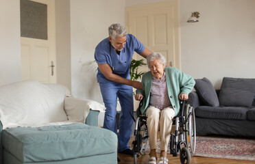 Fototapeta na wymiar Caregiver helping senior woman to stand from her wheelchair in her home.