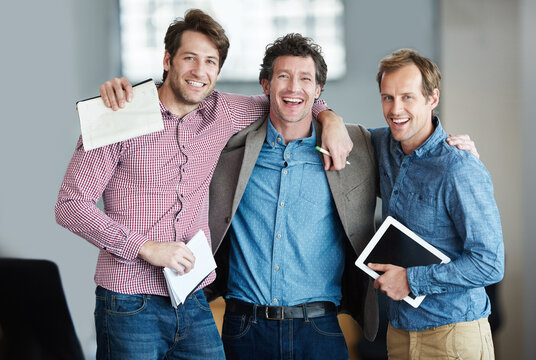 Team, portrait or business developers hug after meeting for support in office together with smile or unity. Confident men, people or happy programmers with technology, notes or notebook in workplace