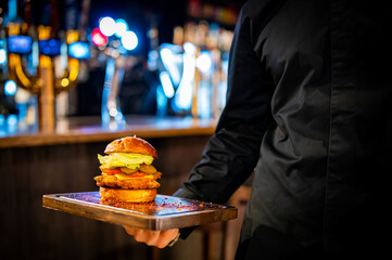 Men's waiter hands hold a tray with a cheeseburger in pub