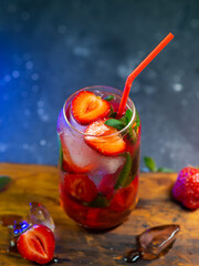 Refreshing strawberry lemonade with ice on a dark table. Ripe berries and mint leaves. Summer strawberry cocktail