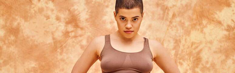 body positivity, curvy and tattooed woman in crop top posing on mottled beige background, looking at camera, representation of body, different body shapes, generation z, youth, banner