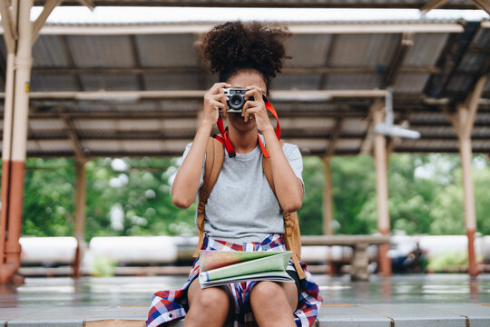 Asian teenage girl african american traveling using a camera take a photo to capture memories while waiting for a train at the station.