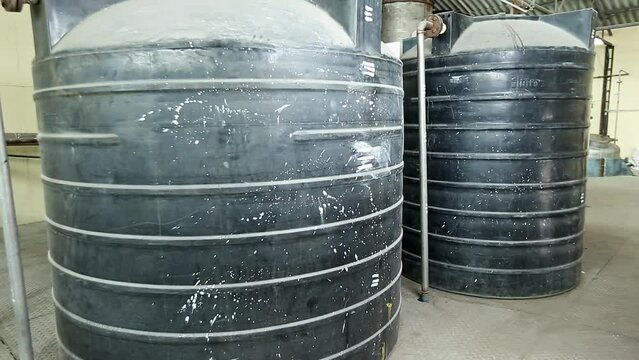 Close-up of old black plastic water tanks with interconnected pipes at the factory