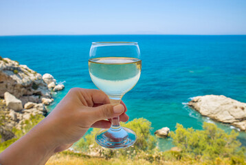 Close up view of woman hand holding glass of white wine with beautiful Rhodes island of Greece...