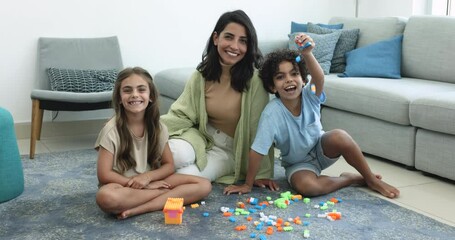 Loving beautiful mother and children portrait, sit on floor, play games enjoy family pastime. Young attractive Brazilian female nanny spend time with siblings. Babysitting job, adoption and custody