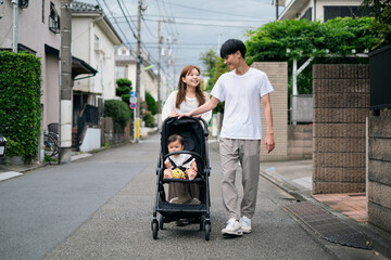 ベビーカーを押しながら赤ちゃんと一緒に散歩する夫婦 - obrazy, fototapety, plakaty