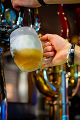 man bartender hand at beer tap pouring beer in glass in bar or pub