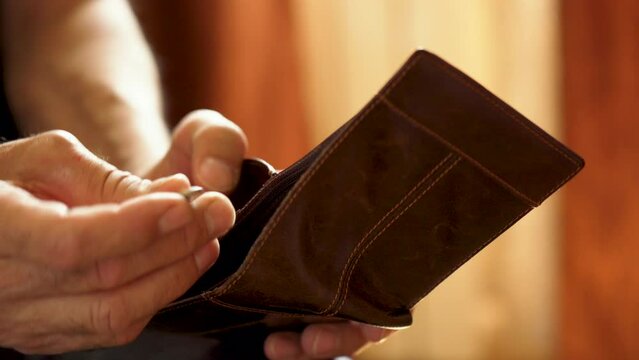 An elderly man's hands, covered with knotted veins, search for coins in his wallet