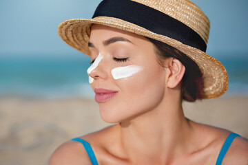 Beautiful Young woman with sun cream on face. Female in hat applying moisturizing lotion on skin.Skin care. Sun protection. Suntan